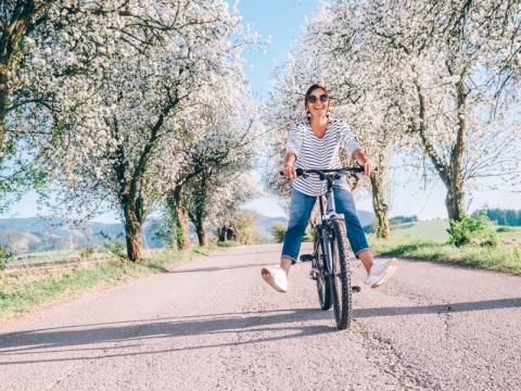 Eine Frau mit Sonnenbrille fährt mit den Fahrrad auf einer Straße und lacht dabei.