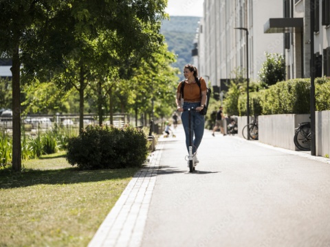 Eine Frau in orangen Shirt auf den Radweg auf einen Scooter.