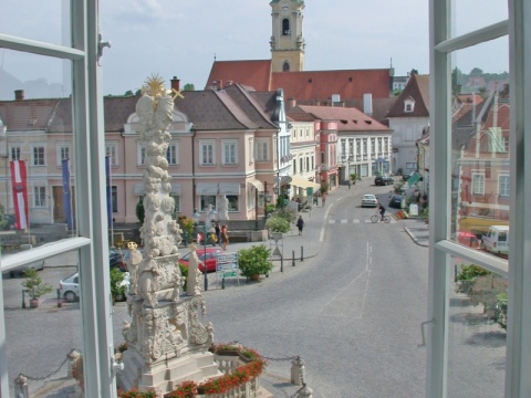 Das Bild zeigt die Innenstadt von Langenlois. Im vorderen Bereich ist die Dreifaltigkeitssäule zu sehen und im hinteren Bereich der Kirchturm.